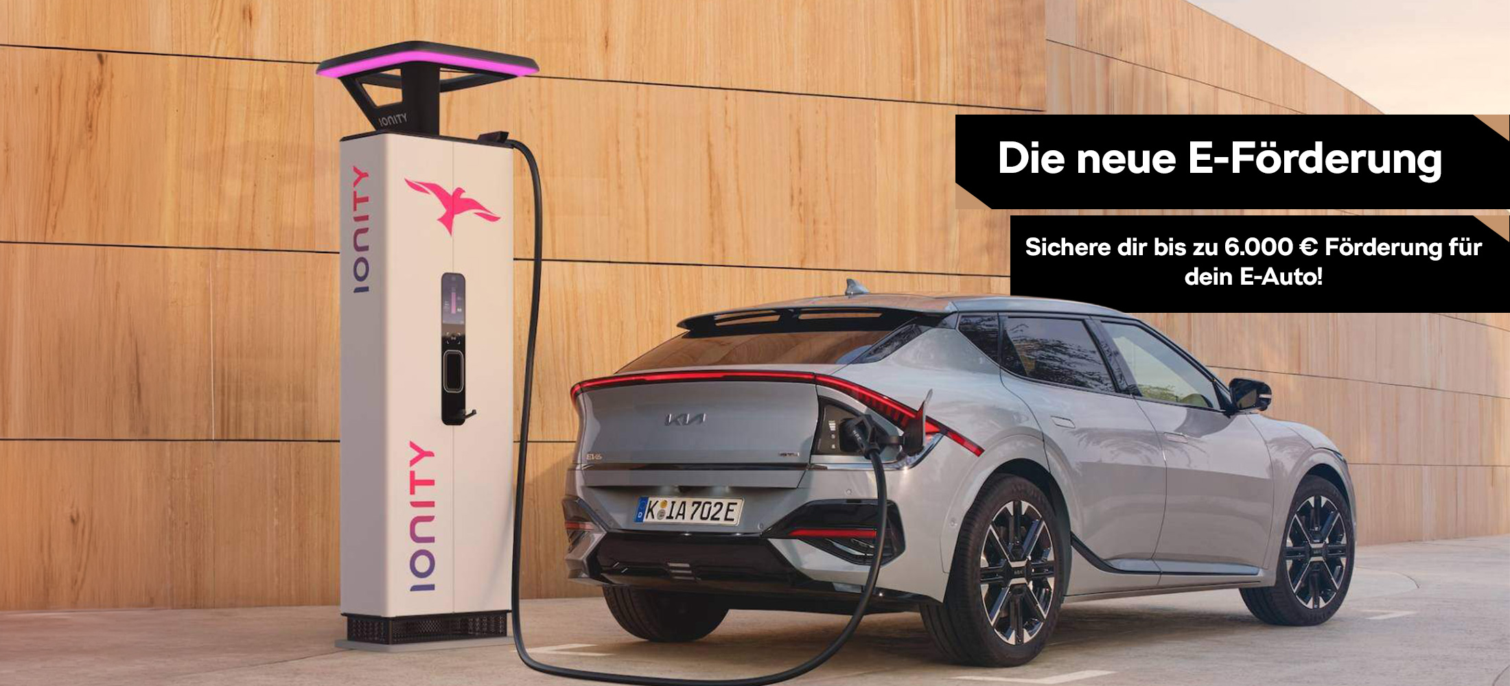 Zwei Kia-E-Modelle stehen auf einer Straße mit Ladegrät im Hintergrund