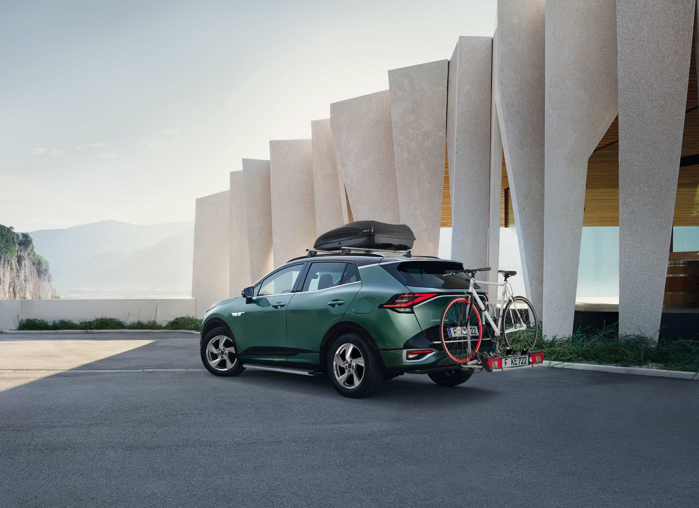 grünes Fahrzeug steht auf einem Parkplatz mit Dachbox und Fahrradträger