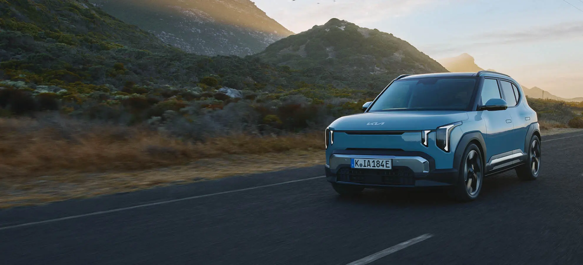 Kia EV2 fahrend auf einer Straße in einer naturellen Landschaft