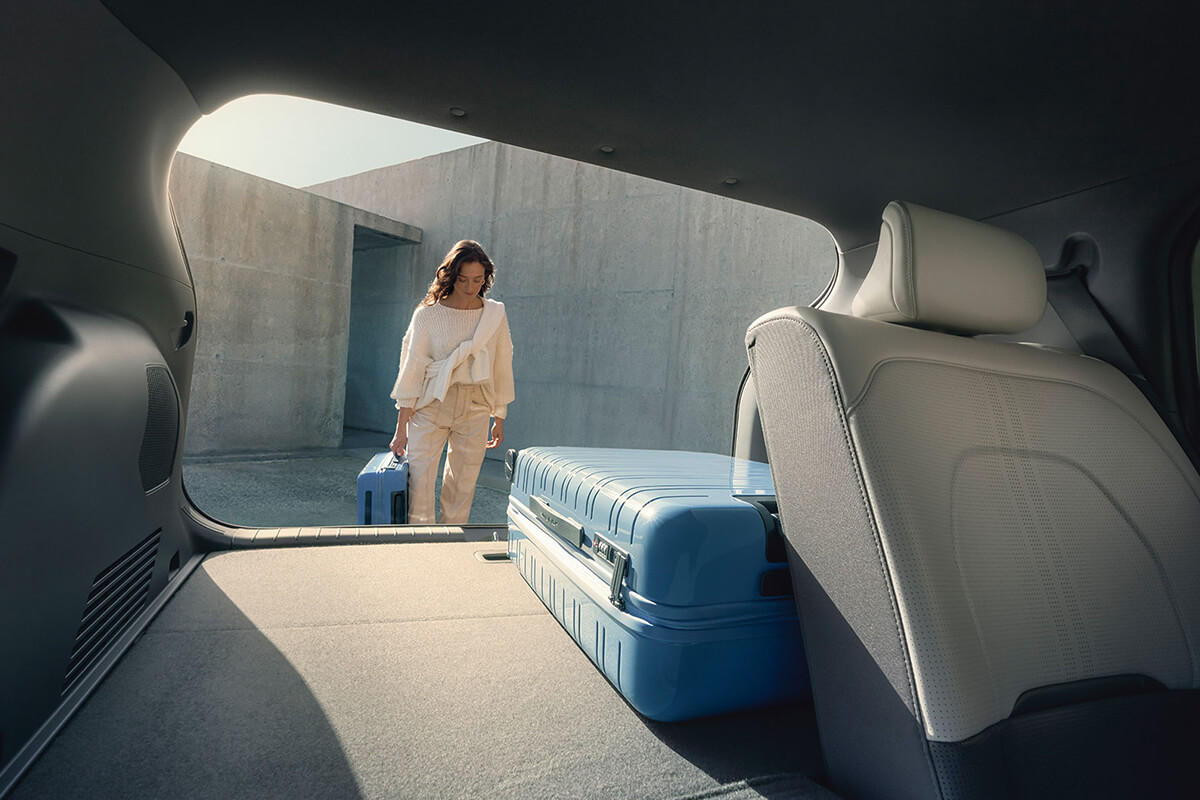 Man sieht den Kia EV3 von innen in Richtung Kofferraum, mit einem Koffer und einer Person, die an der geöffneten Heckklappe steht.